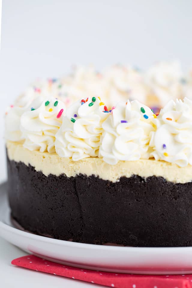 photo showing the side of the cheesecake with the black oreo crust and tall swirls of whipped cream