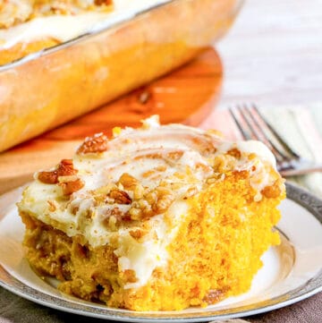 cinnamon roll on a plate with a taupe fabric and a pan of cinnamon rolls behind in