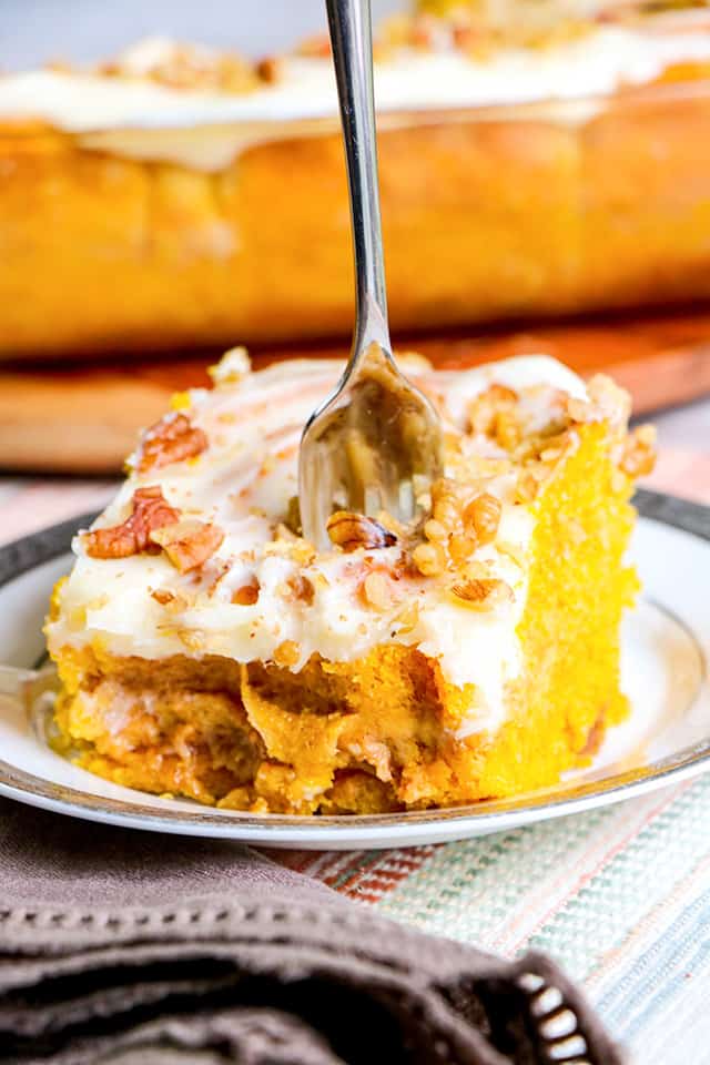 pumpkin cinnamon roll on a silver trimmed plate with a dish of cinnamon rolls behind it