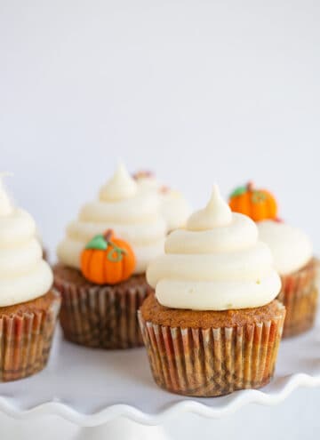 pumpkin cupcakes with swirls of frosting on a wavy white cake plate