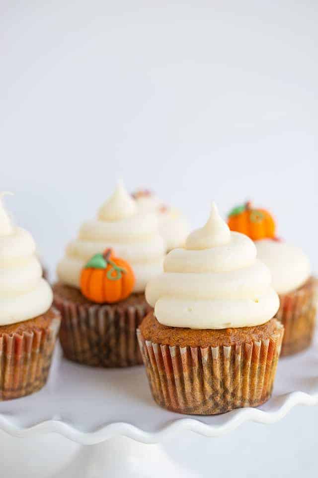 pumpkin cupcakes with swirls of frosting on a wavy white cake plate