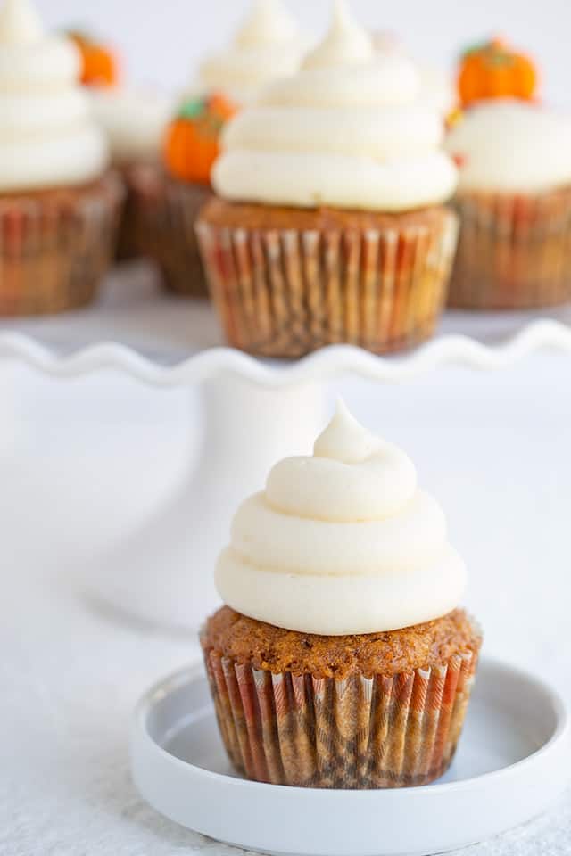 a pumpkin cupcake with a small white plate with a plate full of cupcakes behind it