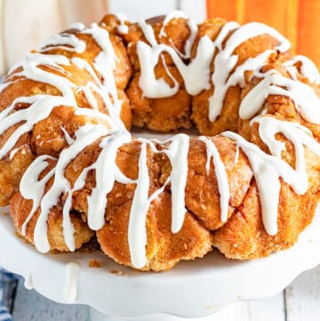 pumpkin spice monkey bread on a white cake plate with pumpkins behind it