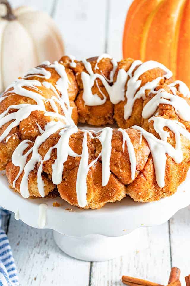 pumpkin spice monkey bread on a white cake plate with pumpkins behind it