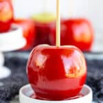 candy apple sitting on a round white plate with other apples behind it