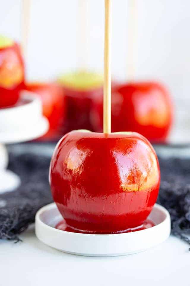 candy apple sitting on a round white plate with other apples behind it