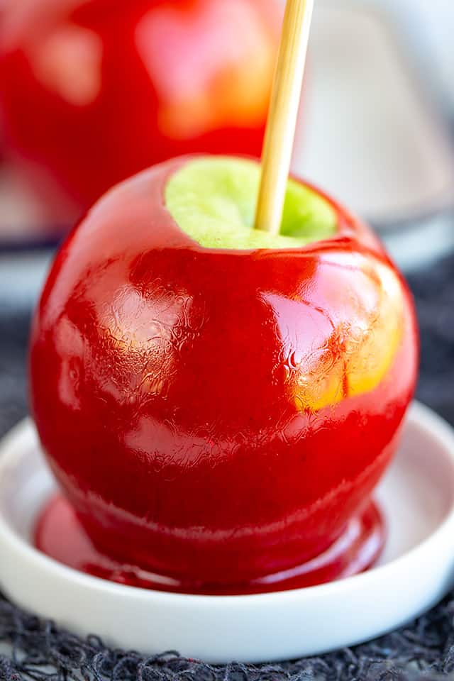 close up photo of candy apple on a white plate with a second apple behind it