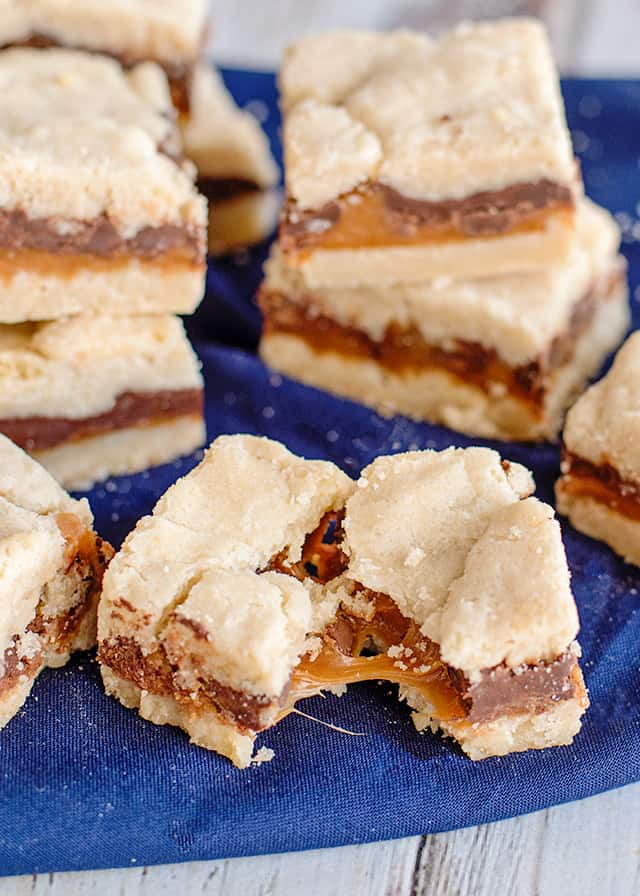 shortbread bars broke in half with the gooey caramel stretching out of it on a blue fabric