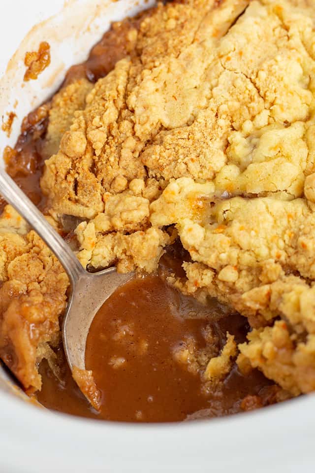 white crockpot full of juice from apple cobbler with spoon in it