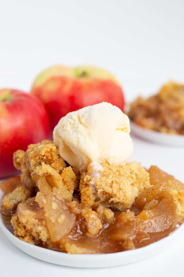 white plate full of slow cooker apple cobbler with vanilla ice cream on top