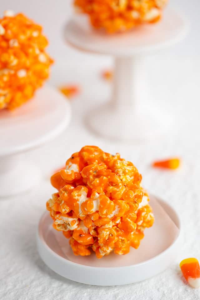 ball of orange popcorn on a white plate with candy corn around it