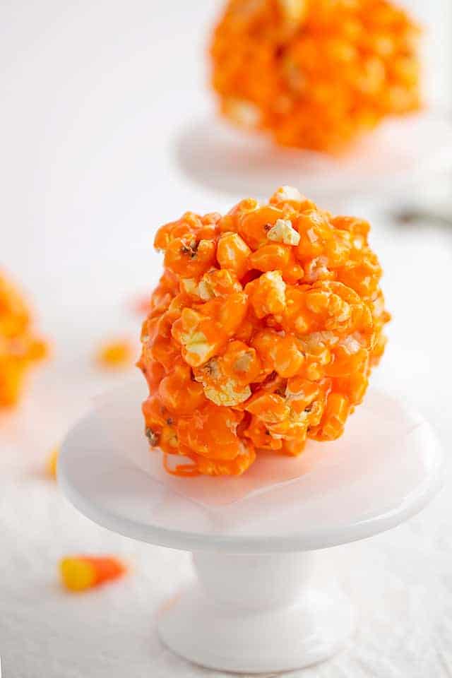 close up of candy corn popcorn ball on a cupcake stand with a second ball behind it