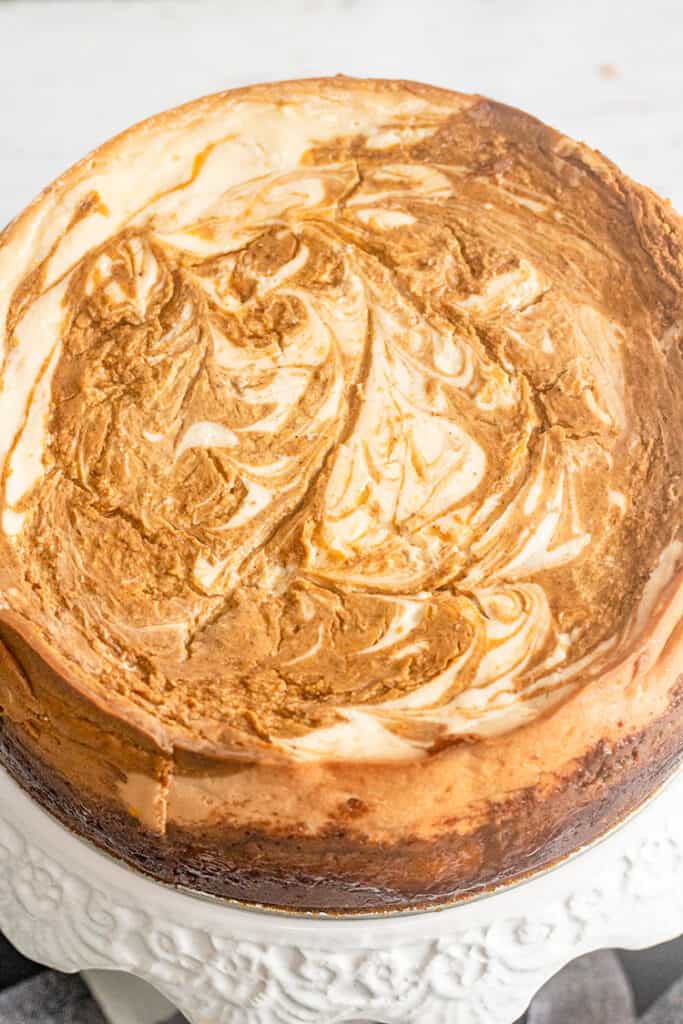 close up of baked pumpkin swirled cheesecake on a white cake plate