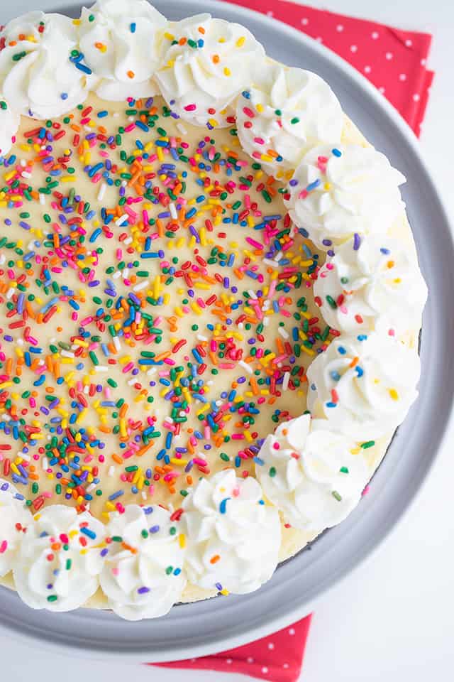 overhead photo of no bake birthday cheesecake on a white plater with a pink fabric