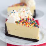 slice of cheesecake on a small white plate with a pink fabric under plate