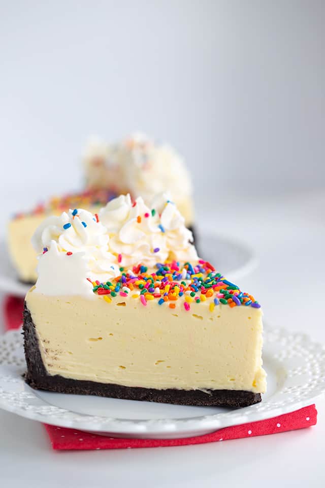 side view of birthday cheesecake with a second slice behind on on a white plate