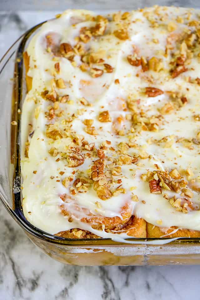 pan of pumpkin cinnamon rolls with a cream cheese frosting in a glass pan on a marble background