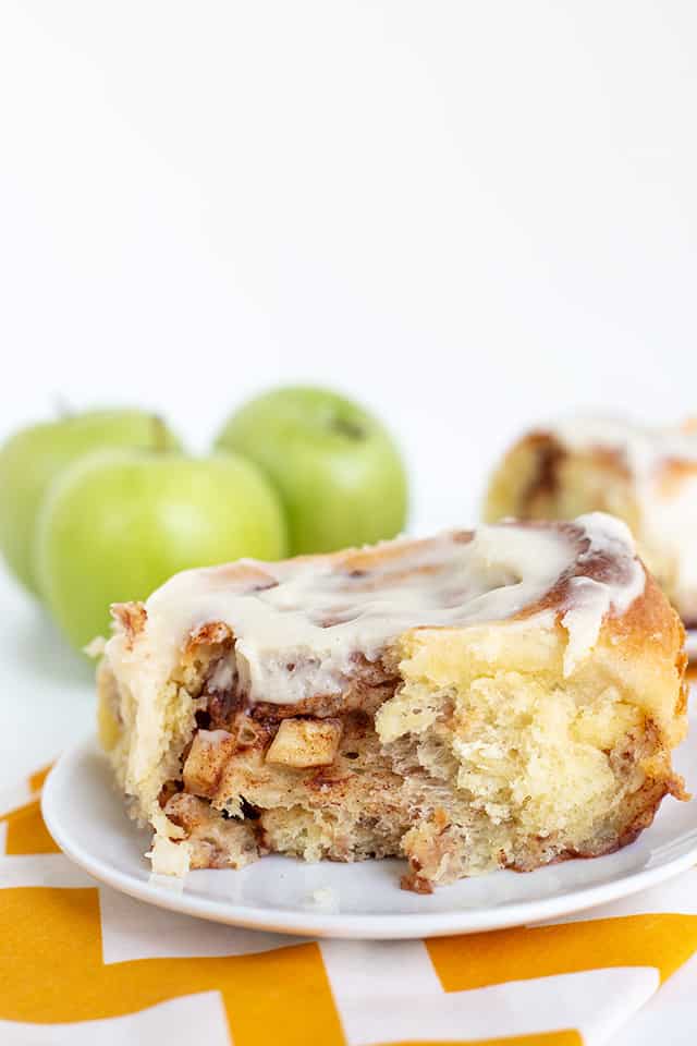 cinnamon roll on a white dessert plate with apples poking out of the cinnamon roll