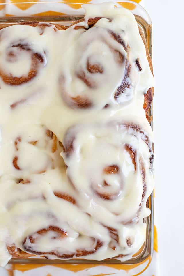 square glass pan of cinnamon rolls with cream cheese icing on top on a white surface