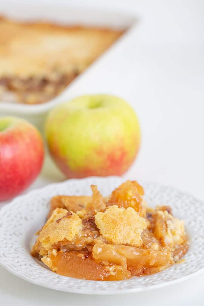 a white lace plate with apple dump cake on it and apples behind it