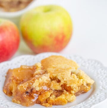 plate full of dump cake with apples behind it and a baking pan