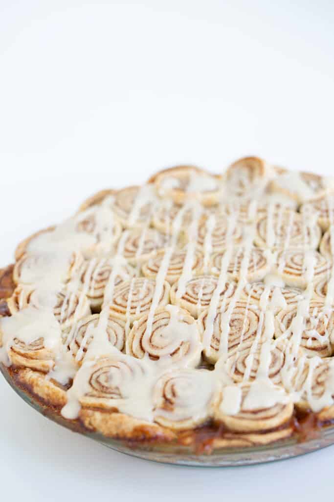 cinnamon roll apple pie in a glass pie dish on a white surface