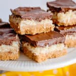 coconut chocolate bars on a white cake plate with a yellow fabric