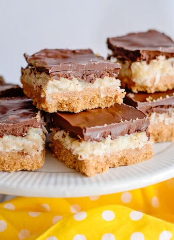 coconut chocolate bars on a white cake plate with a yellow fabric