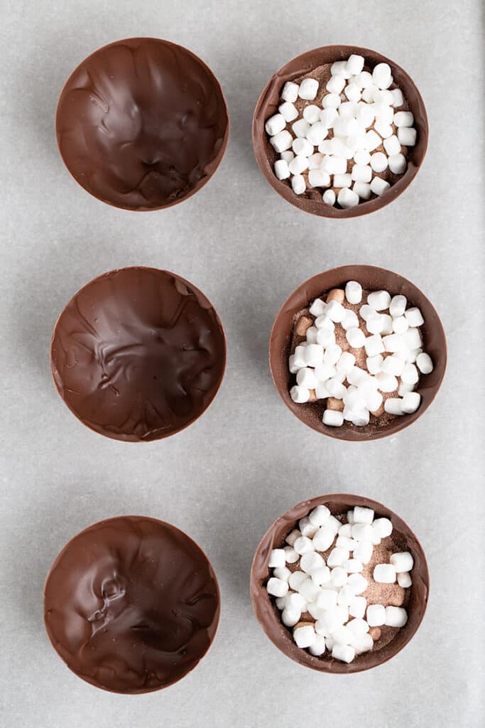 hot cocoa bomb shells with hot cocoa mix and marshmallows in them on parchment paper