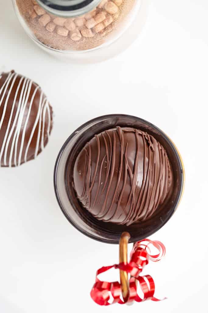 bomb in a glass mug with hot cocoa mix and a second chocolate bomb beside it