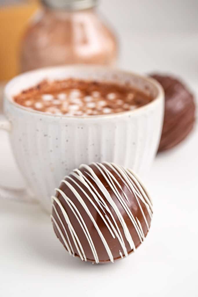 hot chocolate bomb in front of a white mug filled with hot cocoa