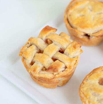 mini apple pie with lattice crust on a white platter with a green apple in the background