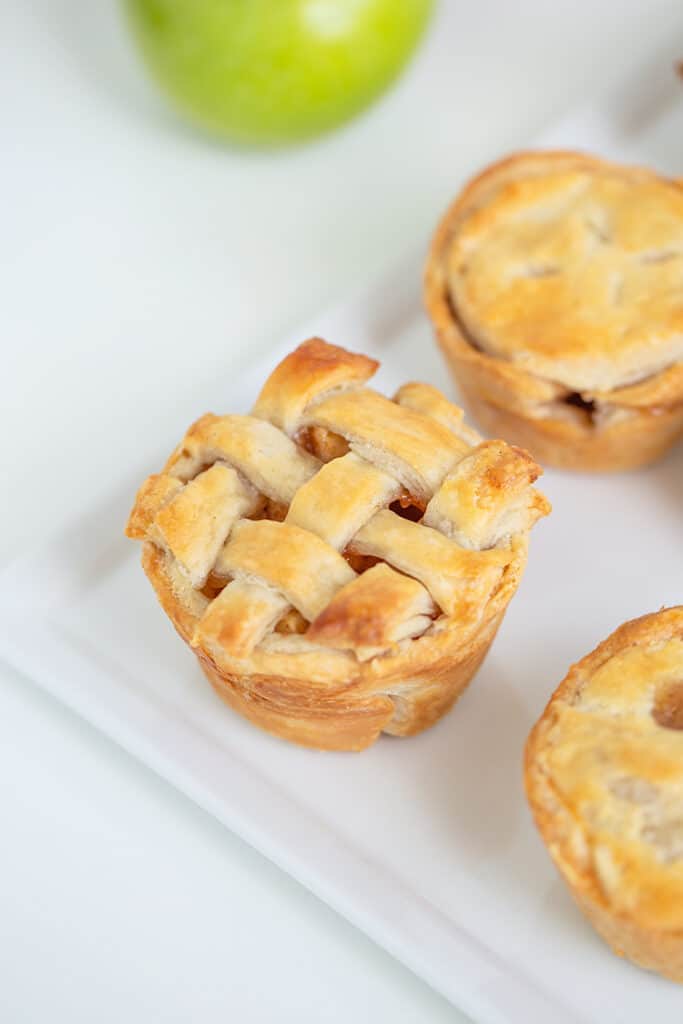 mini apple pie with lattice crust on a white platter with a green apple in the background