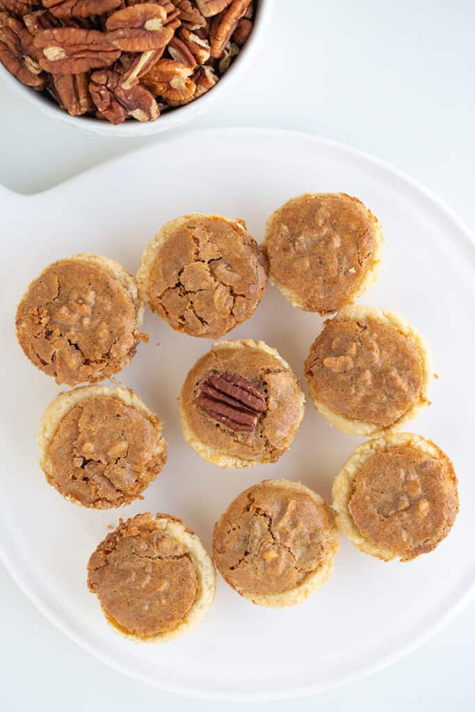 white platter with pecan tassies on it and a bowl of pecans beside it