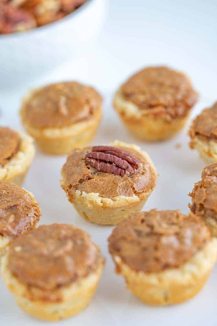 showing the middle pecan tassie with a whole pecan on it on a white surface