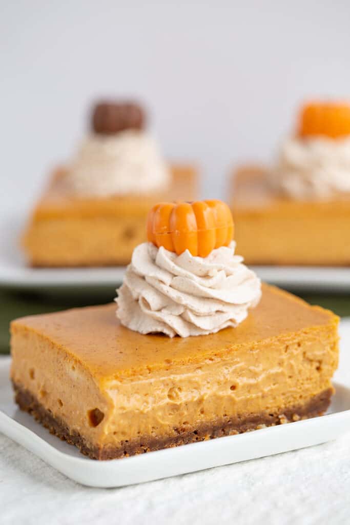 close up of a slice of cheesecake bars with whipped cream and a pumpkin on top