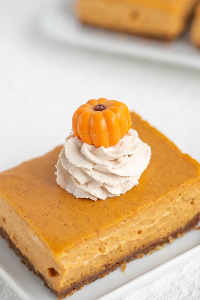 cheesecake bars showing the pumpkin truffle on top of the whipped cream that's sitting on the pumpkin bar