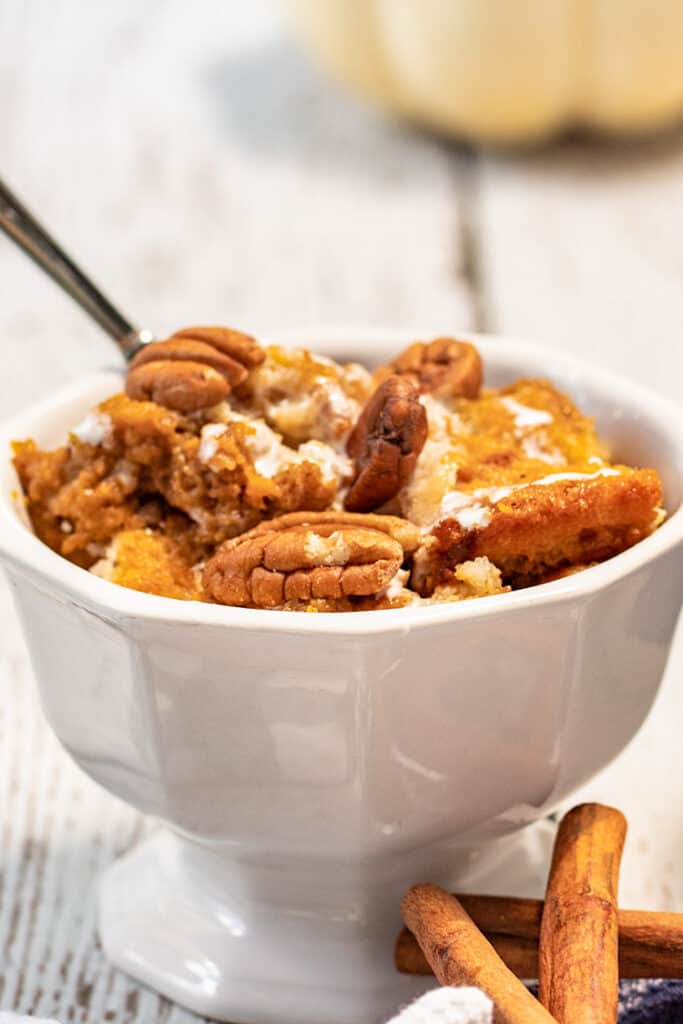 white serving dish full of pumpkin cobbler with a spoon and cinnamon sticks