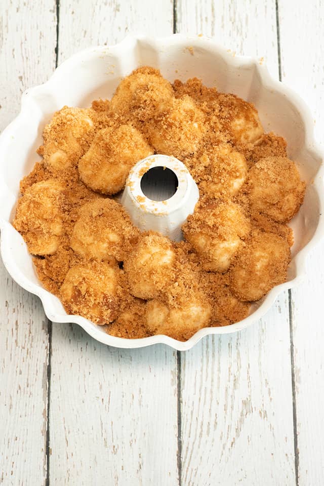 cinnamon sugar covered dough balls in a bundt pan on a white wooden surface