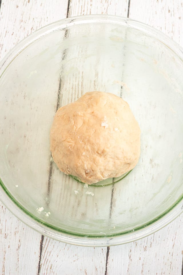 ball of dough in a large glass bowl under a white wooden surface