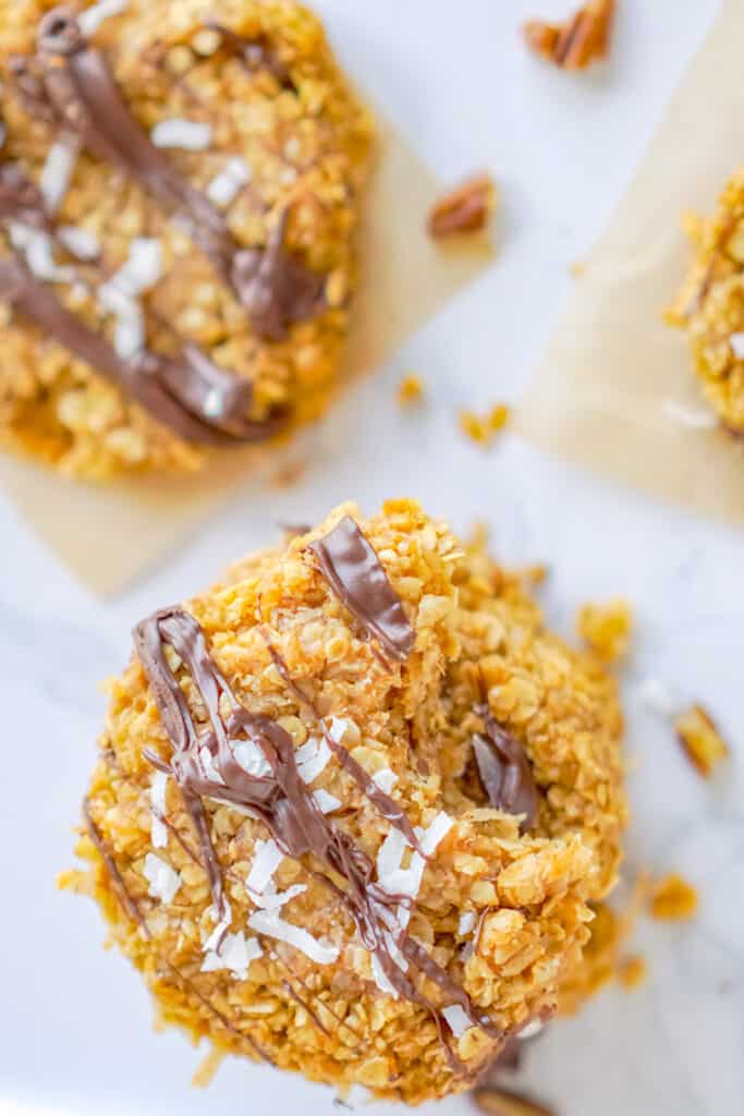 close up of the no bake cookies with coconut and chocolate drizzled on top on parchment paper