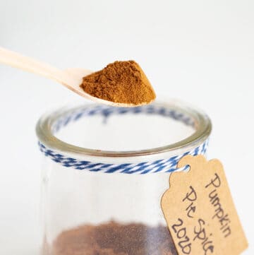 wooden spoon full of pumpkin pie spice above a glass jar of pumpkin pie spice