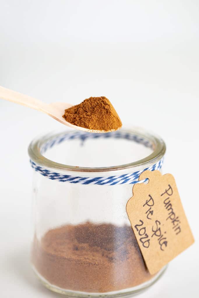 wooden spoon full of pumpkin pie spice above a glass jar of pumpkin pie spice