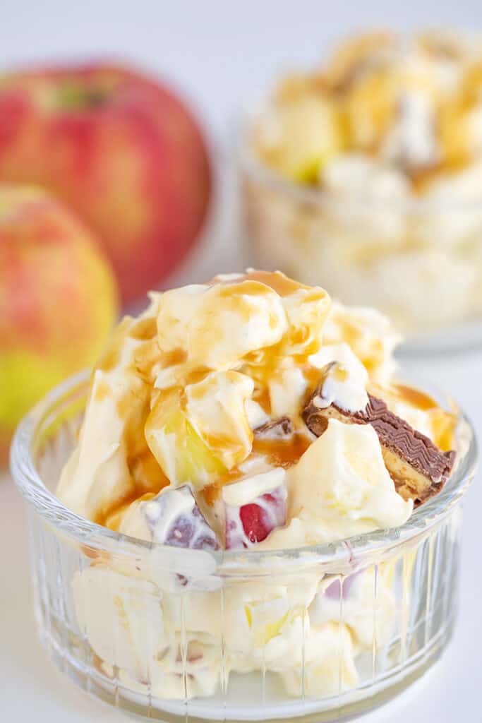 glass bowl full of snickers salad with apples behind it