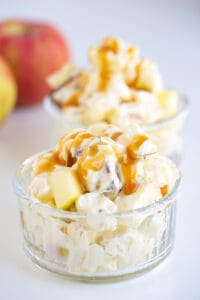 glass bowl full of apple salad on a white surface with apples behind it