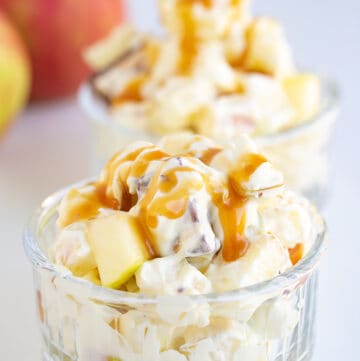 glass bowl full of apple salad on a white surface with apples behind it