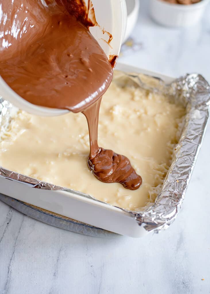 pouring melting chocolate on the sweetened condensed milk and coconut layer of the bars