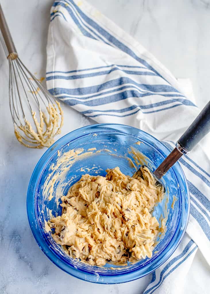 a blue mixing bowl full of potoato chip cookie dough with a white and blue fabric