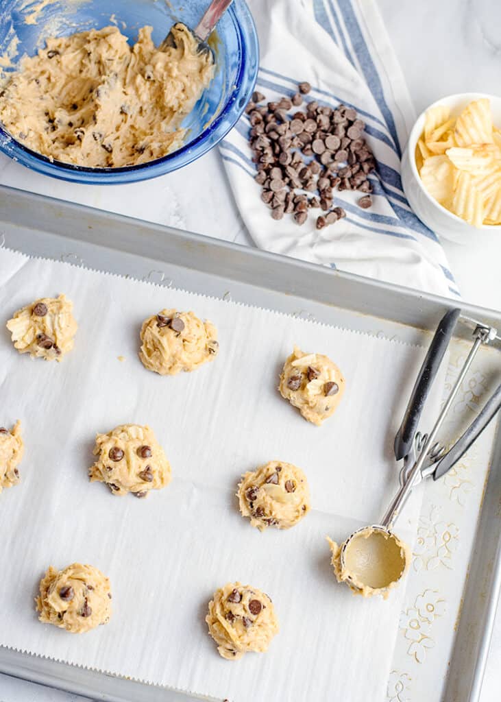 scoops of cookie dough on a piece of parchment paper with a cookie scoop beside it