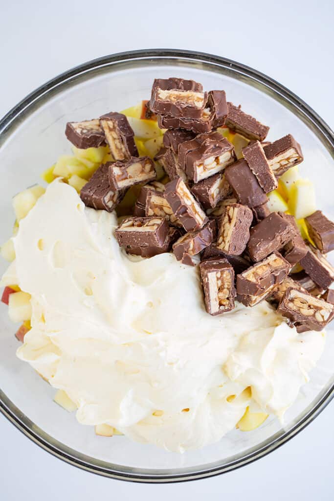 bowl full of snickers, cream cheese pudding filling, and chopped apples on a white surface